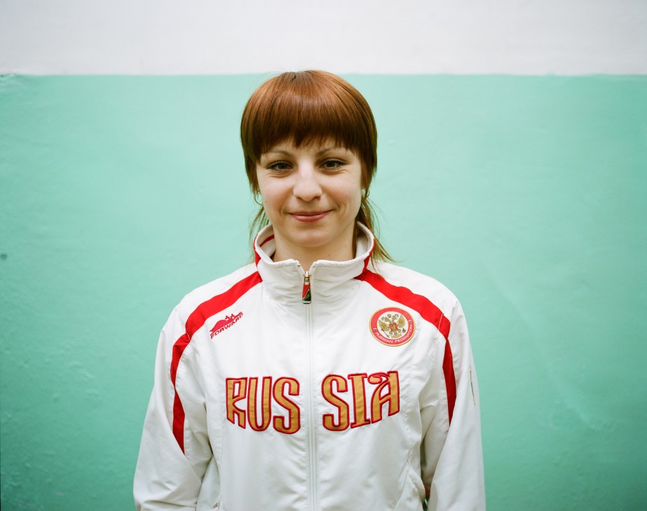 Woman in white and red Russian tracksuit with wushu champion emblem against turquoise background