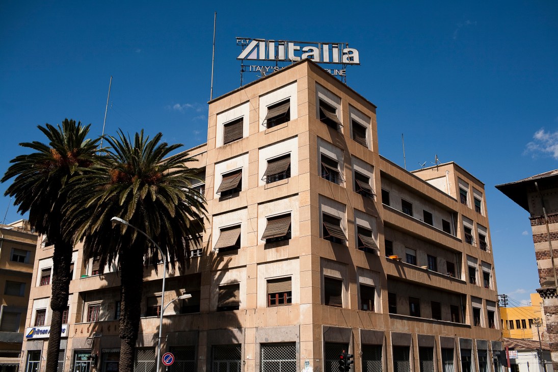 Italian colonial architecture in Asmara with Alitalia airline sign on rooftop and palm tree.