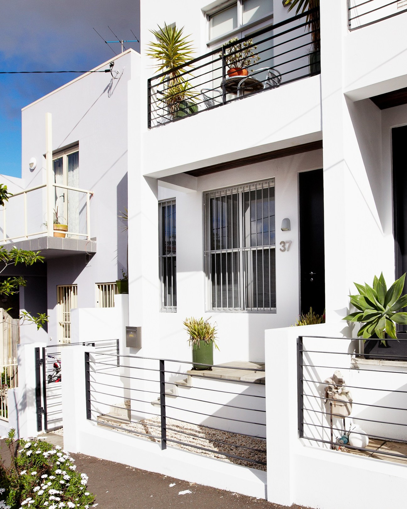 Modern white townhouse with black metal railings, potted plants, and multi-level balconies in Erskineville.
