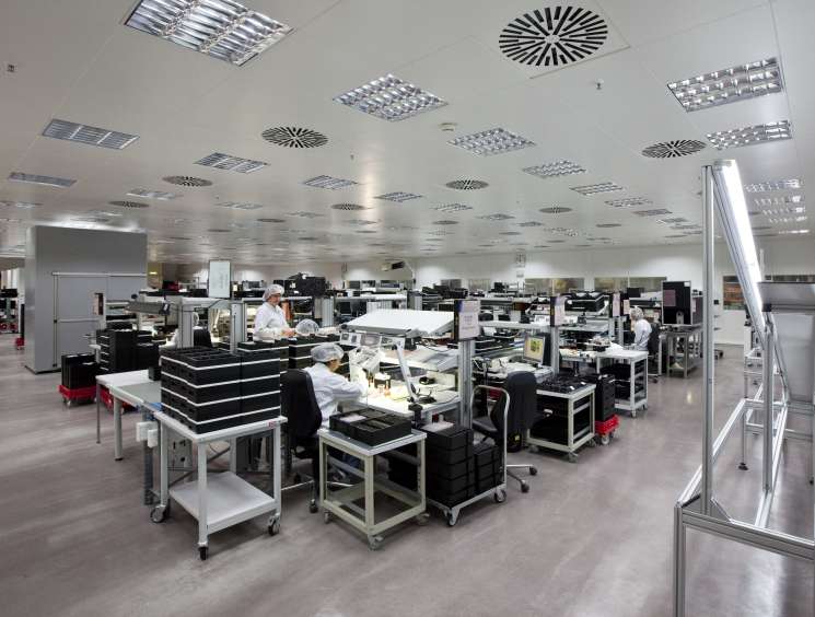Workers assembling camera components at Leica manufacturing facility with precision workstations.
