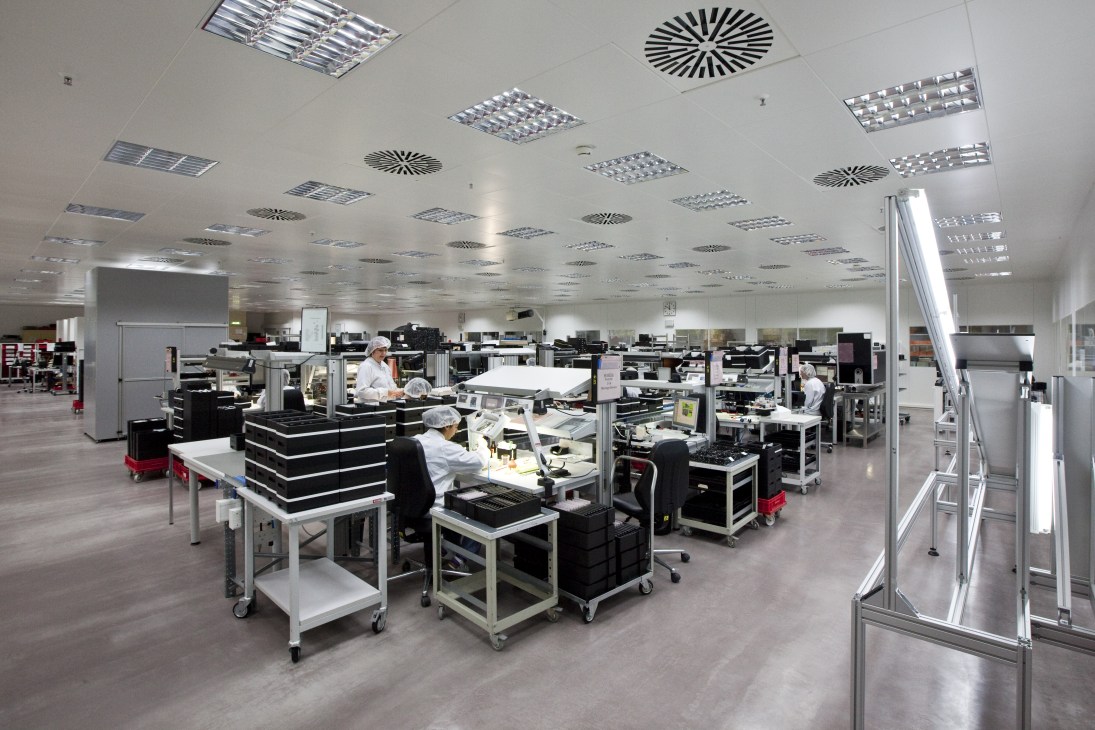 Workers assembling camera components at Leica manufacturing facility with precision workstations.