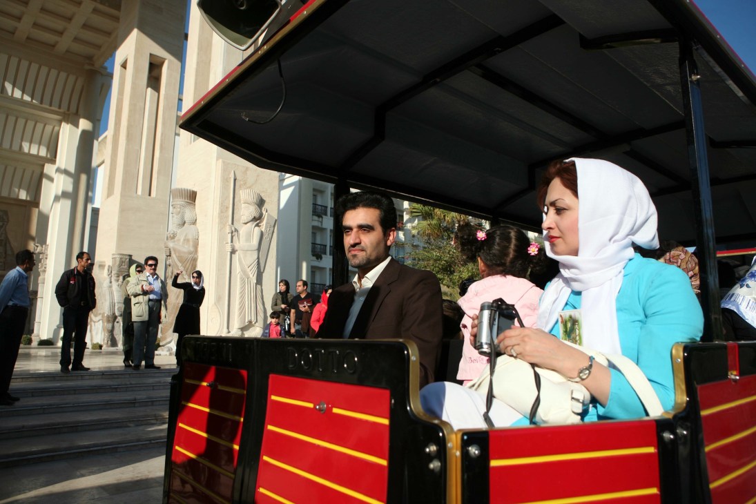 Tourists riding in a red tourist train in front of the Dariush hotel with Persian architectural details visible.
