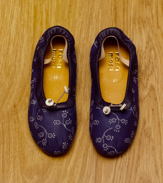 Pair of handmade Rosa Mosa women's shoes with indigo-dyed blue fabric and yellow wooden lasts, displayed on wooden floor.
