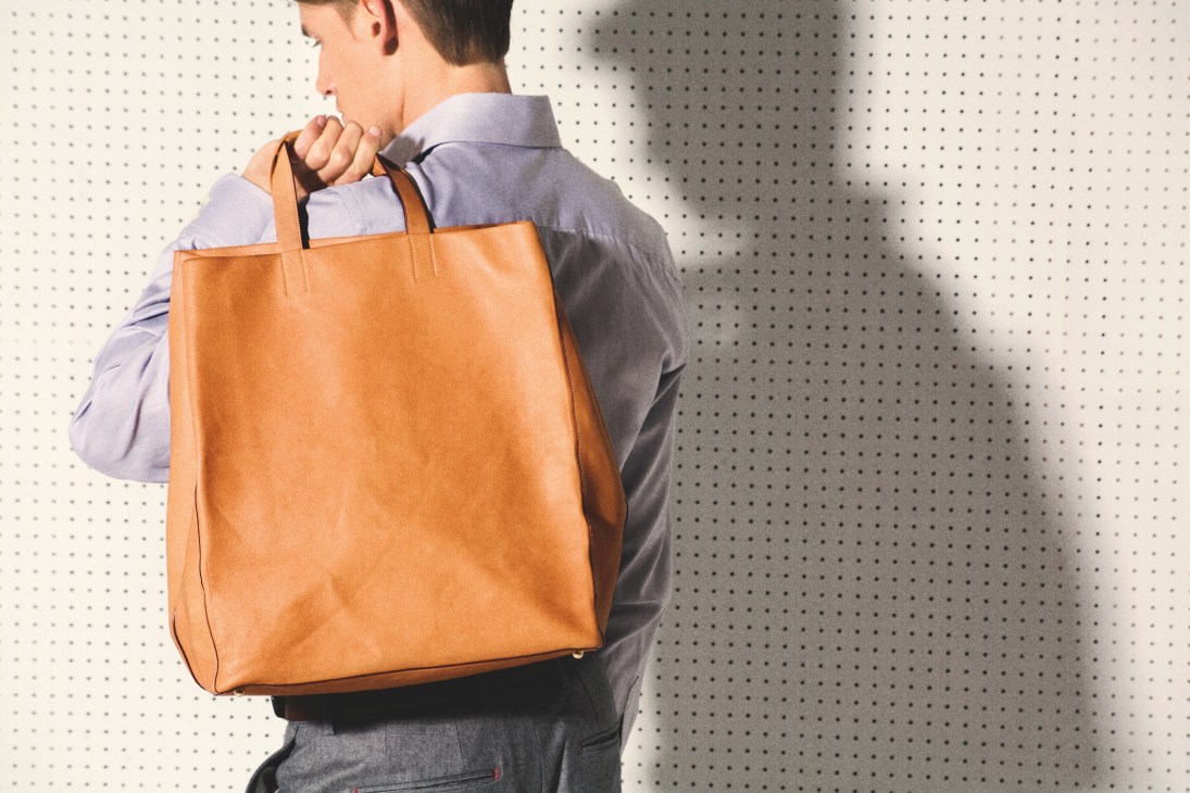 Man wearing tan nappa leather Loewe Papelle bag over shoulder with protective flap.
