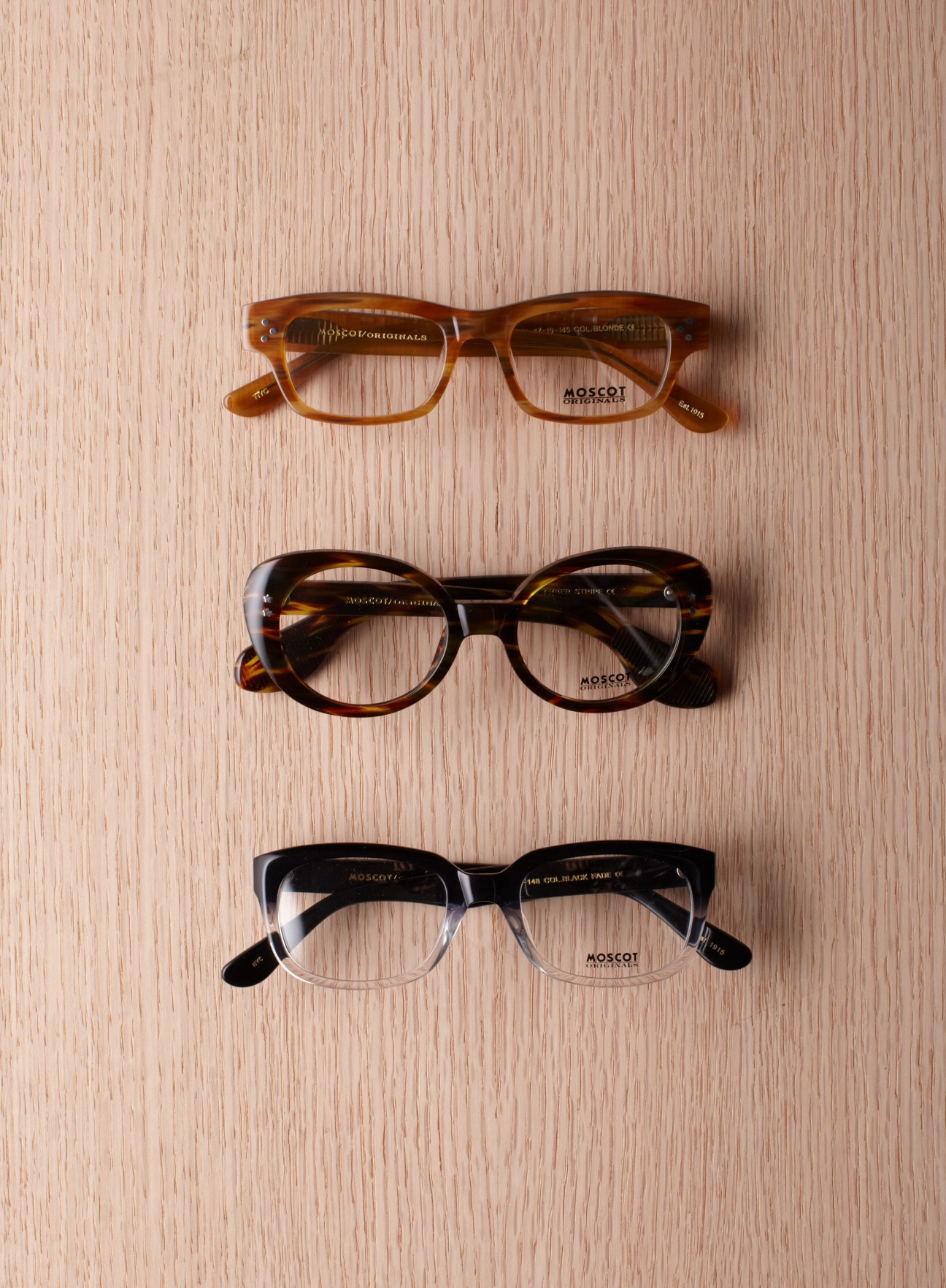 Three pairs of Moscot optical frames in different styles and colors arranged on a wooden surface.