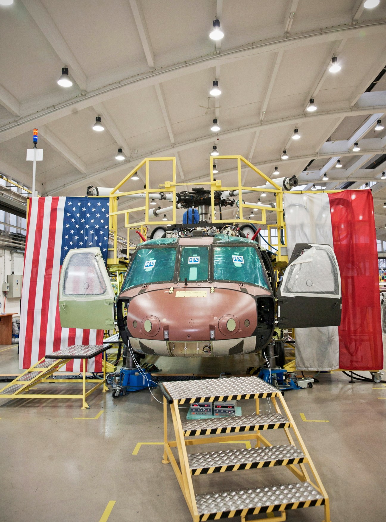 Black Hawk helicopter under construction in factory with US and Polish flags displayed on either side.