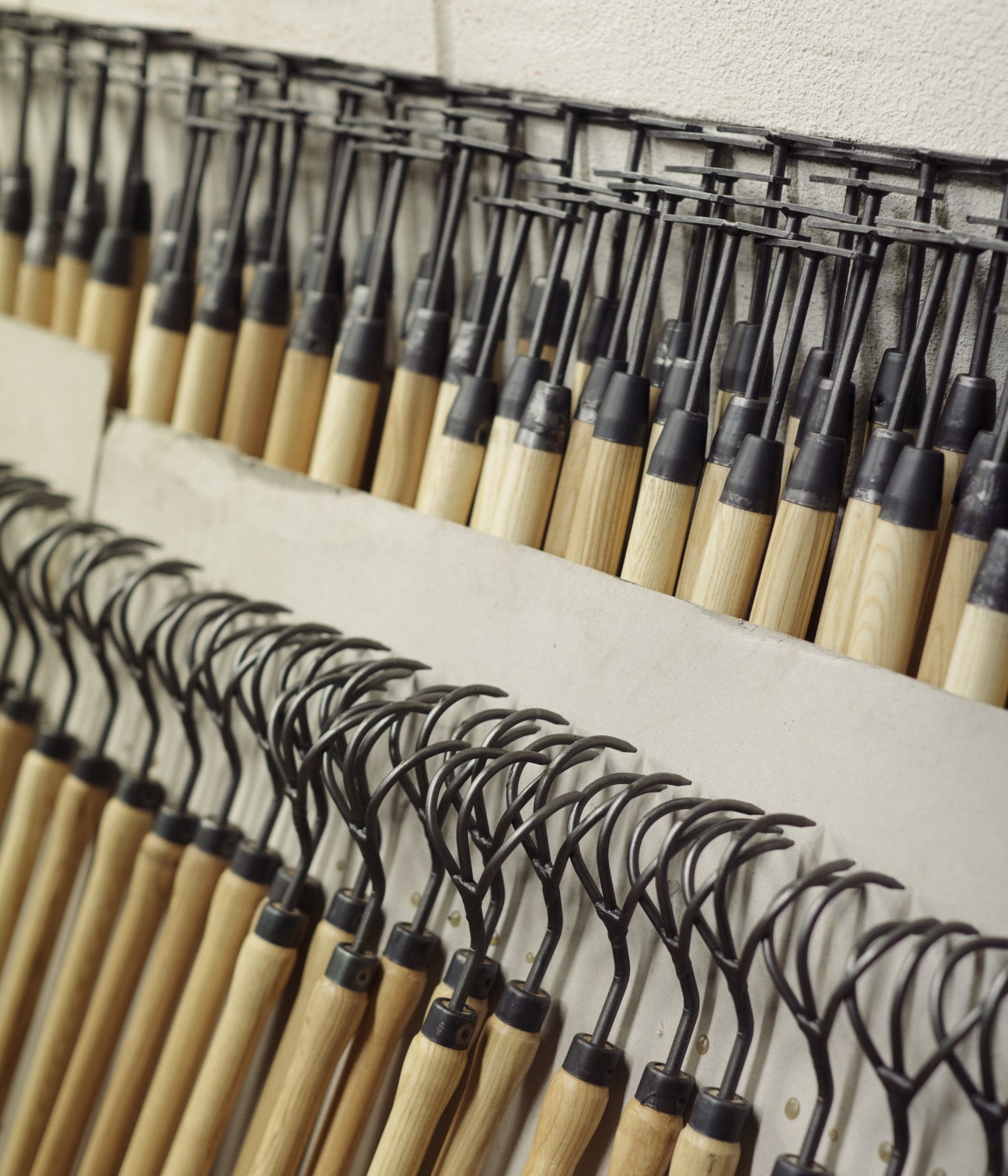 Rows of garden tools with wooden handles and metal heads hanging on display racks.