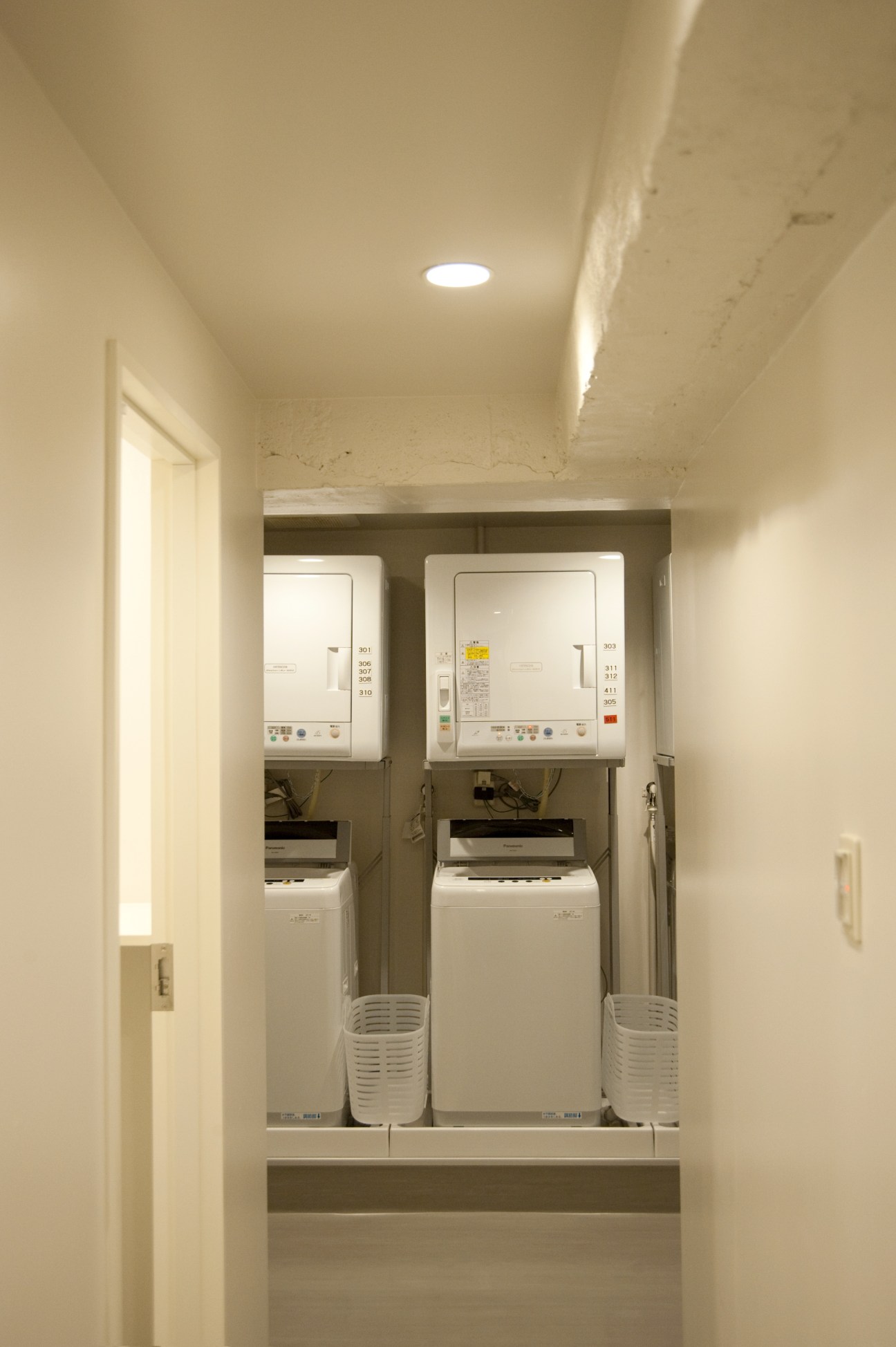 Two white washing machines and dryers in a clean, minimalist laundry room with recessed lighting.