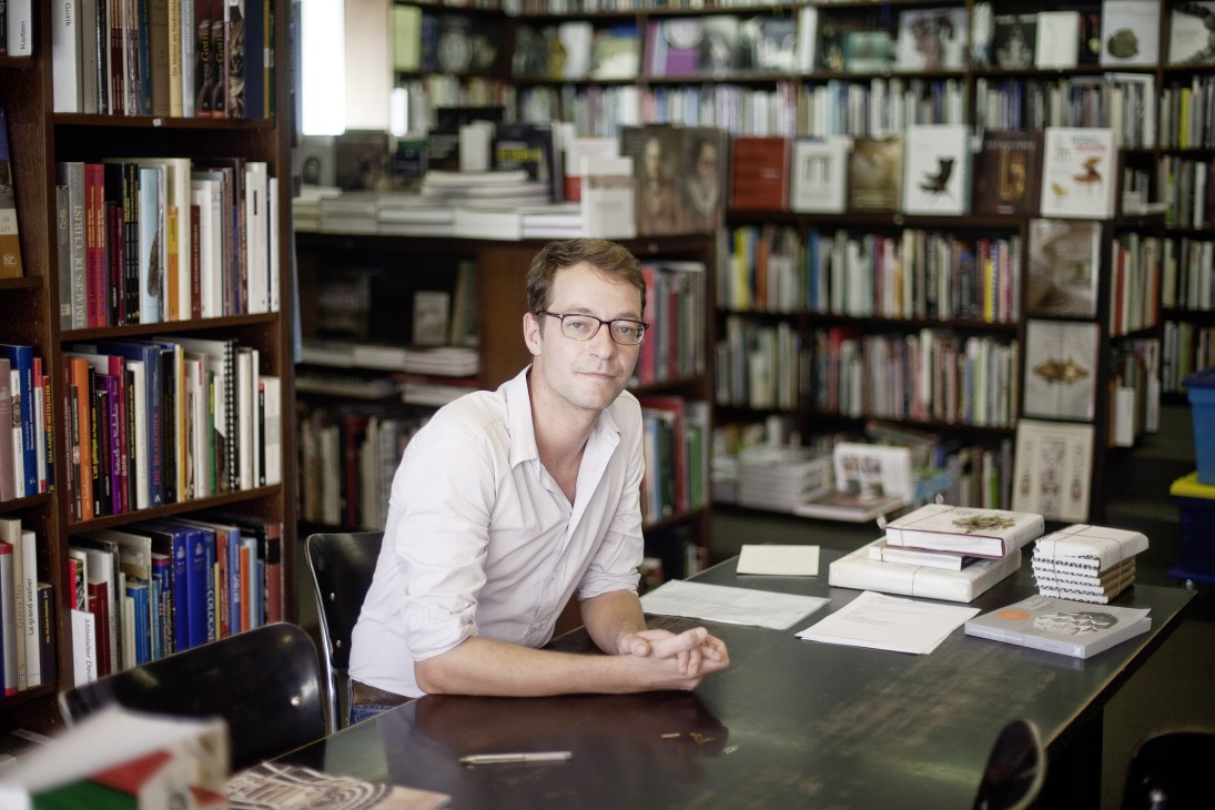 Franz Koenig, owner of Koenig bookshop, seated at a desk surrounded by books and shelving.
