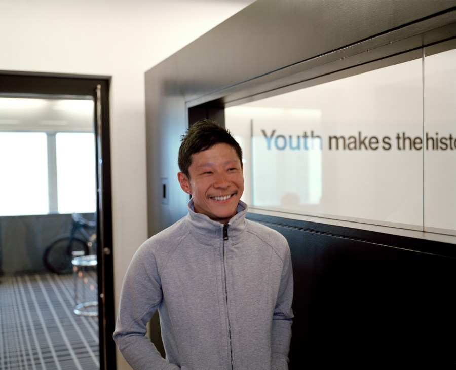 Yusaku Maezawa, founder of Start Today, smiling in the company's office with a whiteboard behind him.
