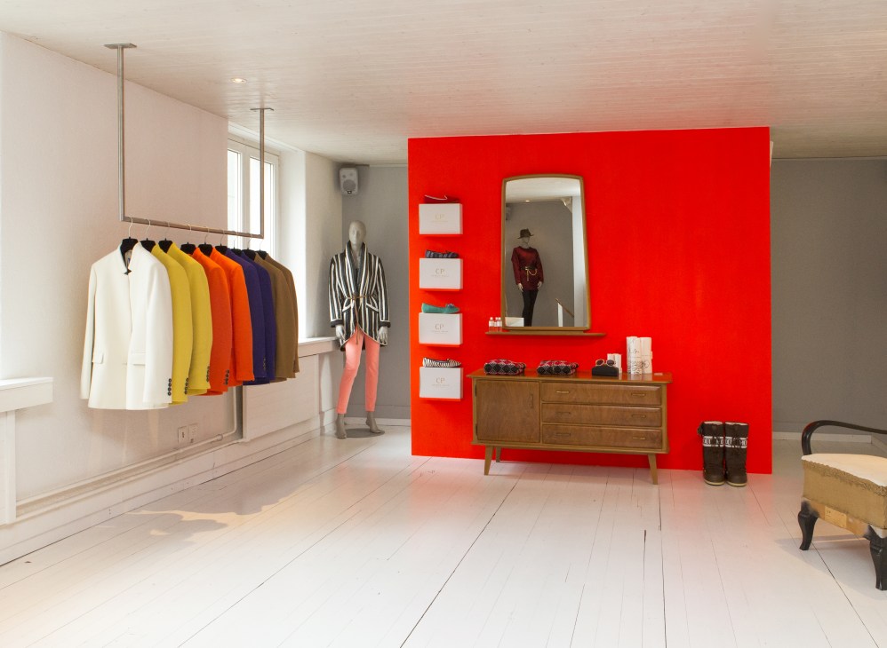 Minimalist fashion retail interior with colorful jackets on rail and red feature wall displaying menswear.