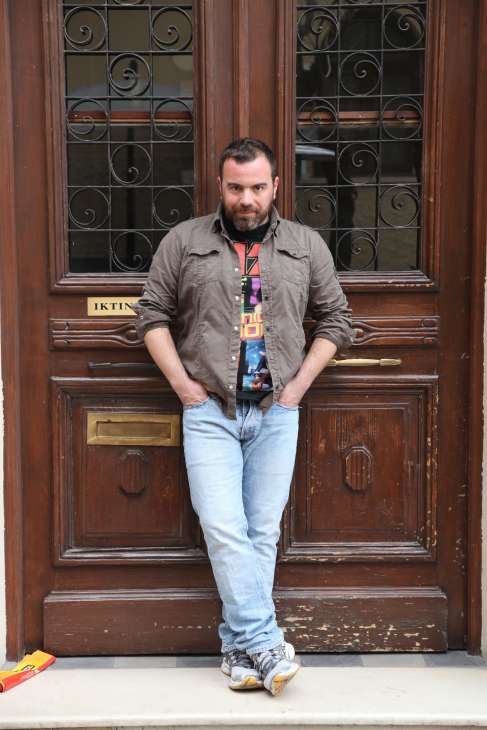 Chef Vasilis Kallidis stands in front of a wooden door with ornate ironwork in Athens.