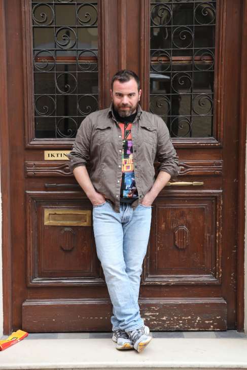 Chef Vasilis Kallidis stands in front of a wooden door with ornate ironwork in Athens.