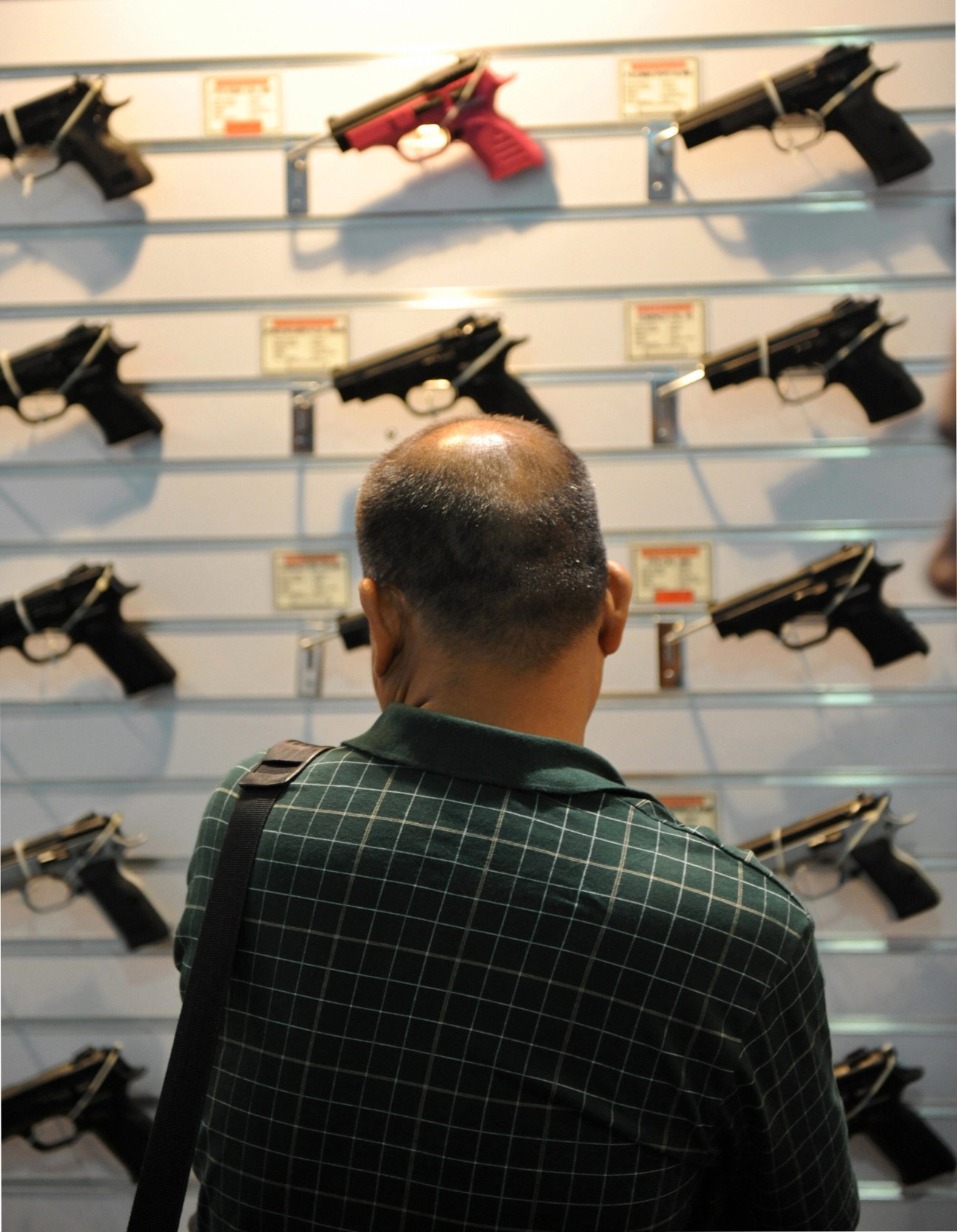 Person viewing handguns displayed in a store window case.