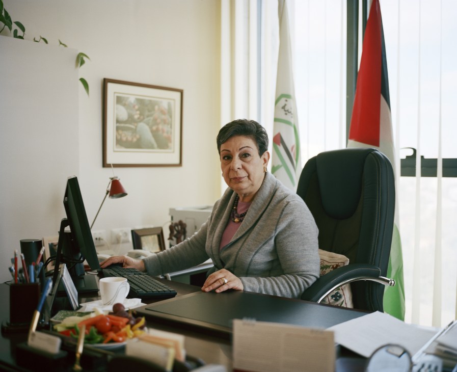 Hanan Ashrawi sits at her desk in an office with Palestinian flags visible in the background.