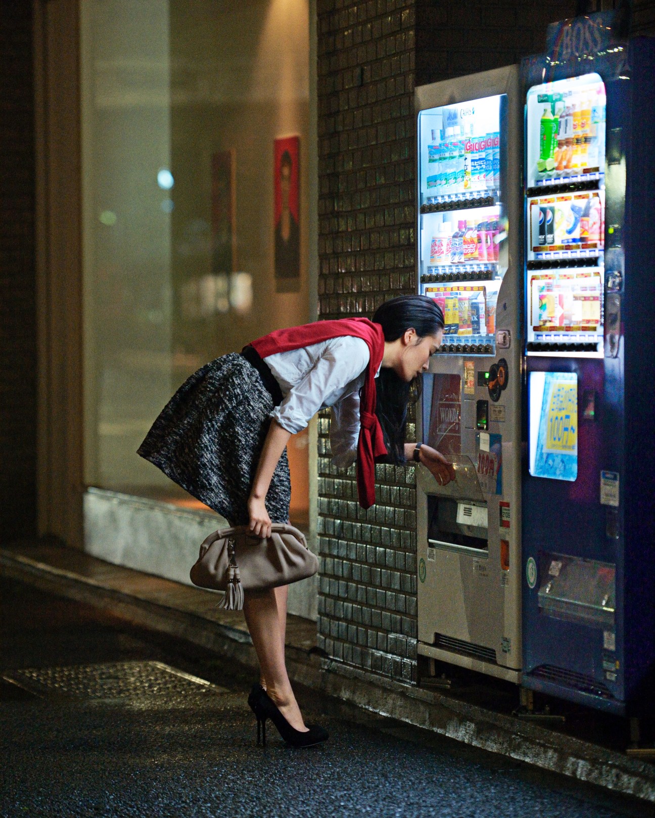 Woman in designer clothing using a Japanese vending machine at night.