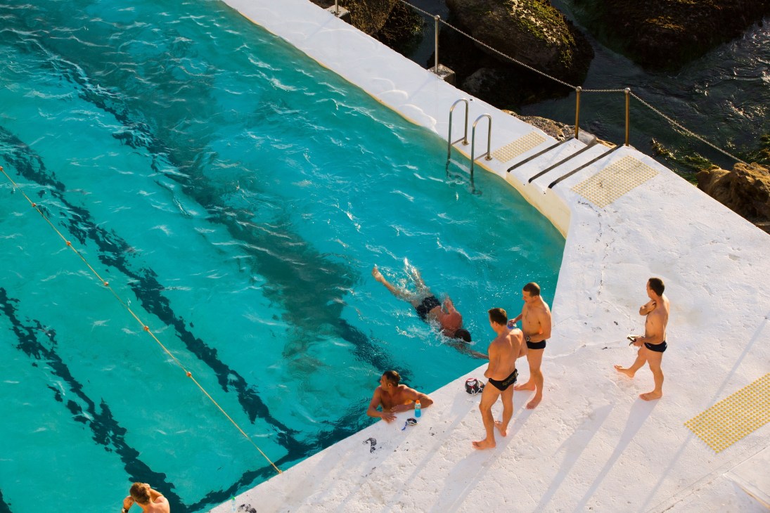 Children standing on the pool deck at Bondi Icebergs, with swimmers doing laps in the turquoise sea pool.