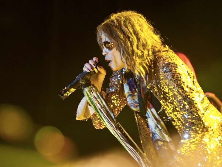 Heavy metal singer performing on stage wearing a gold sequined jacket and sunglasses.