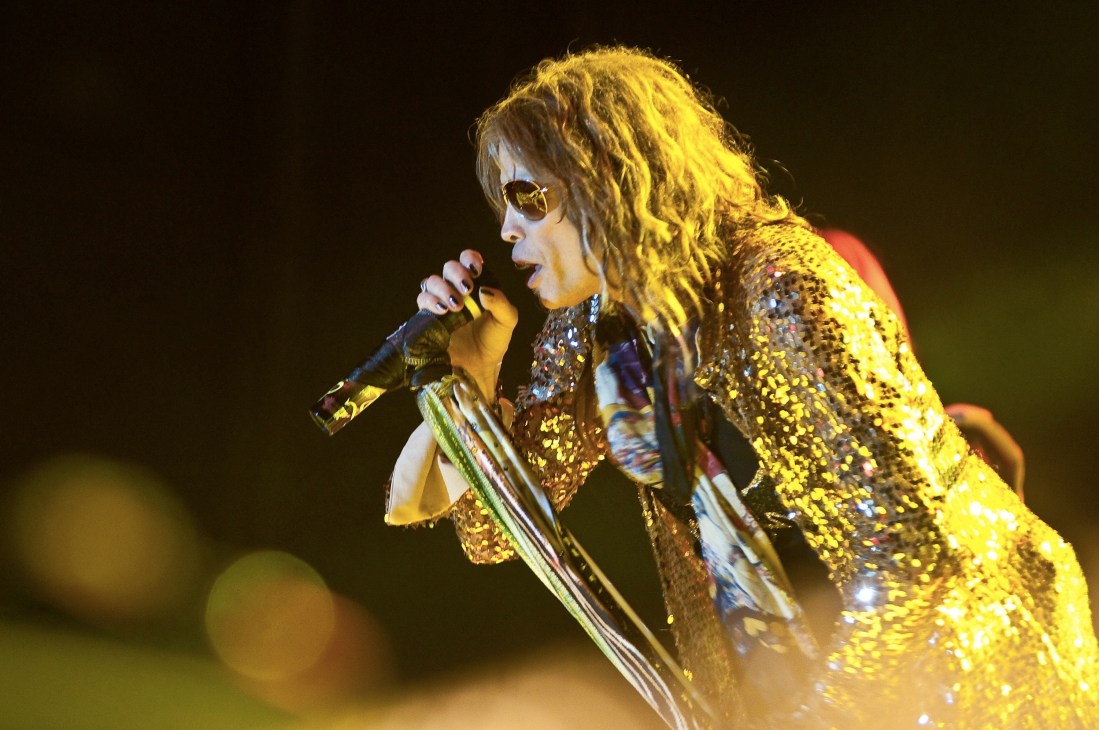 Heavy metal singer performing on stage wearing a gold sequined jacket and sunglasses.