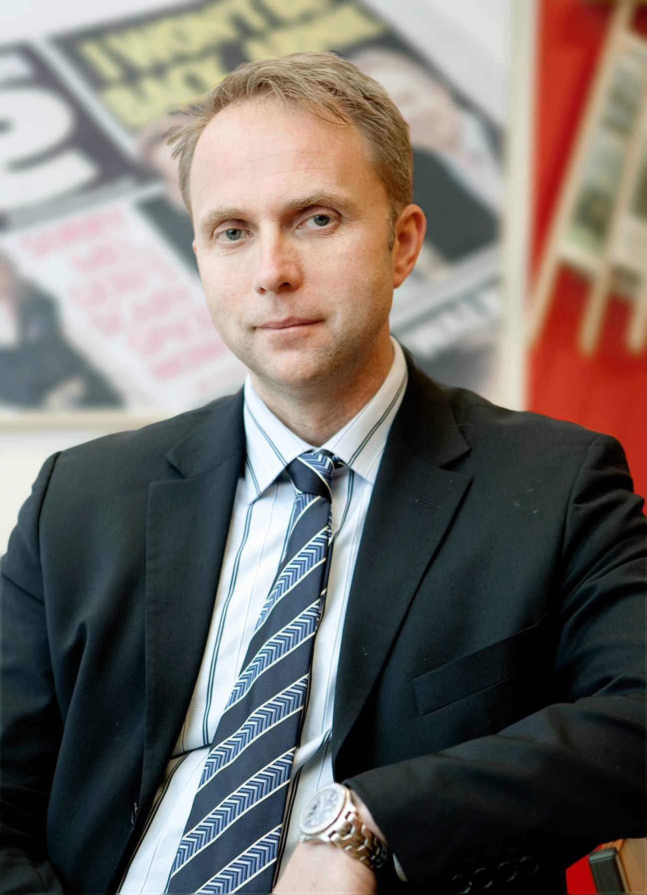 Jan Melin, CEO of Tolerans, wearing a dark blazer and patterned tie, poses for a portrait with newspapers visible in the background.