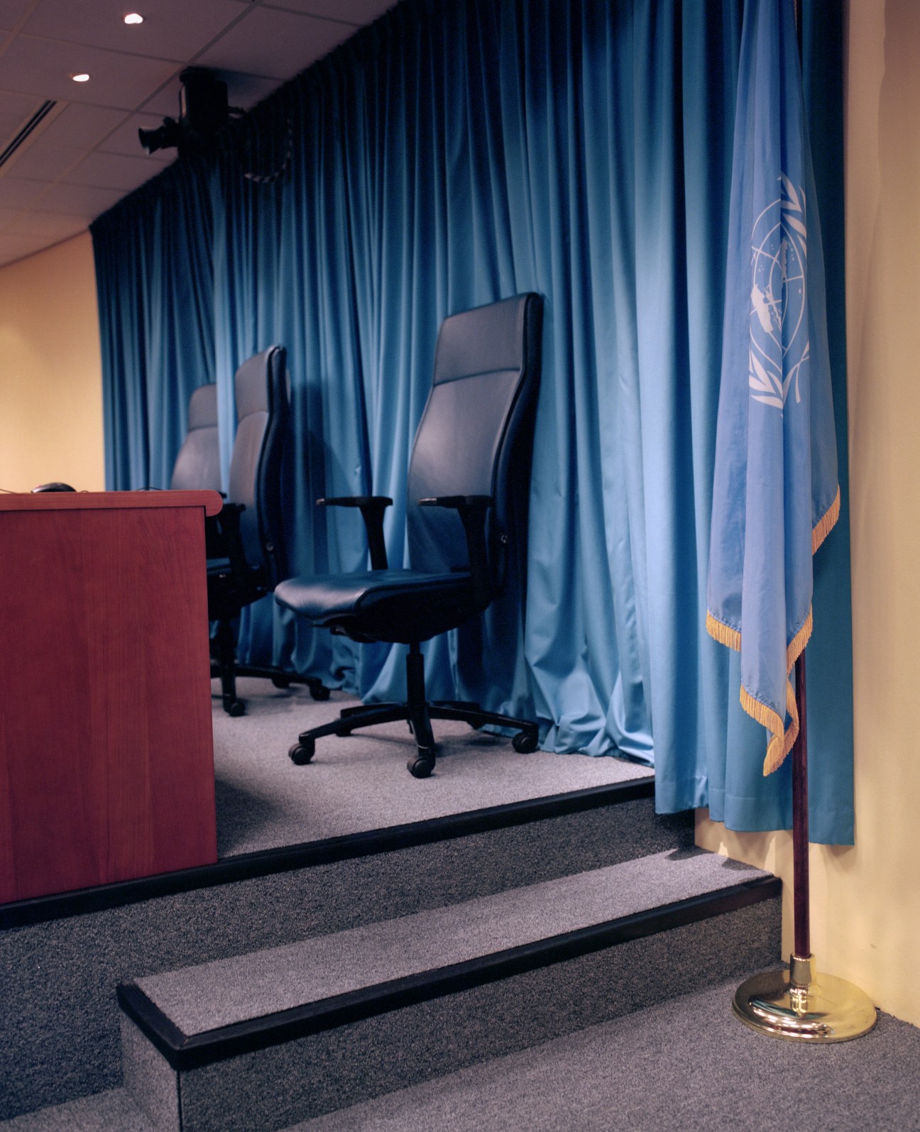 Empty judges' bench with two black chairs behind blue curtains and UN logo at the International Criminal Tribunal for the former Yugoslavia in The Hague.