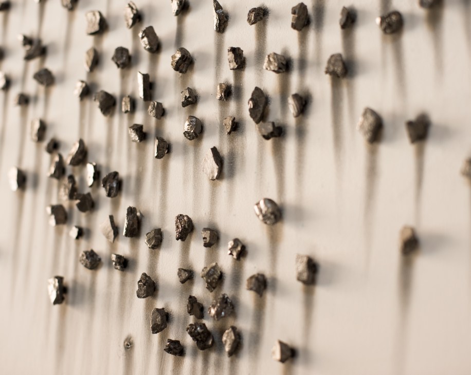 Close-up of Teresita Fernández's artwork 'Epic' showing scattered dark graphite chunks on a white surface.