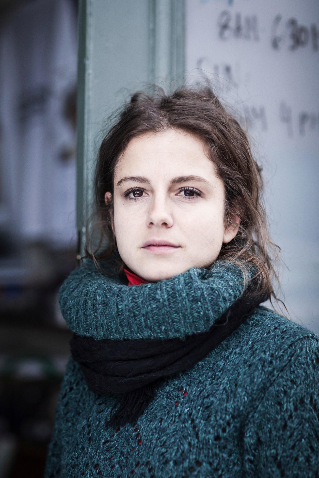Portrait of a woman wearing a teal knit sweater and red scarf against a blurred urban background.