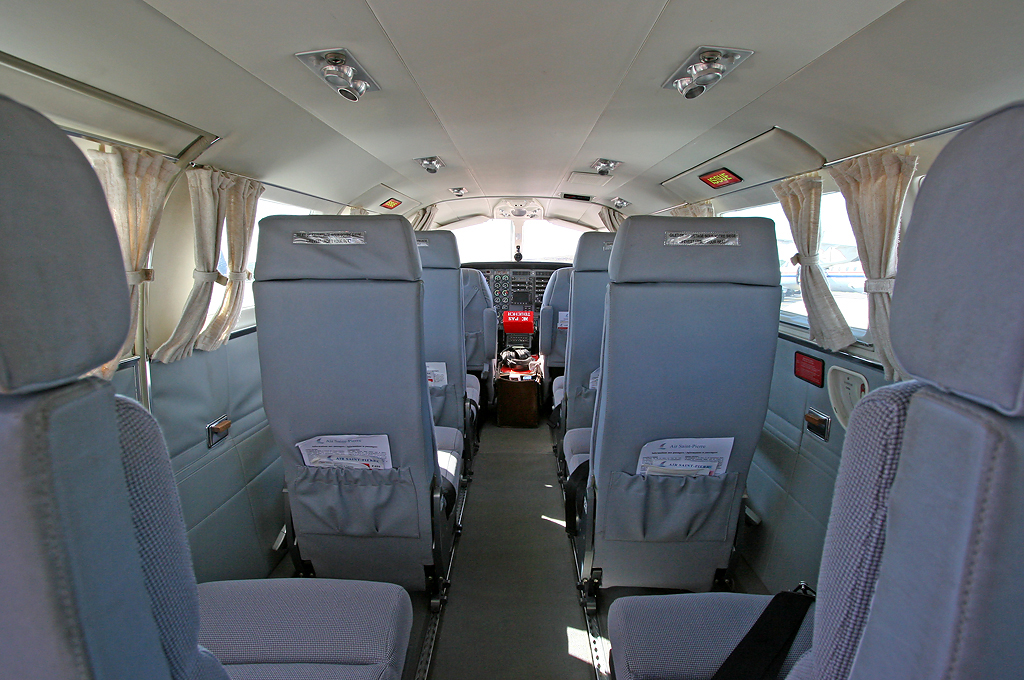 Interior of Air Saint-Pierre aircraft showing blue seats, aisle, and cockpit forward view with windows.