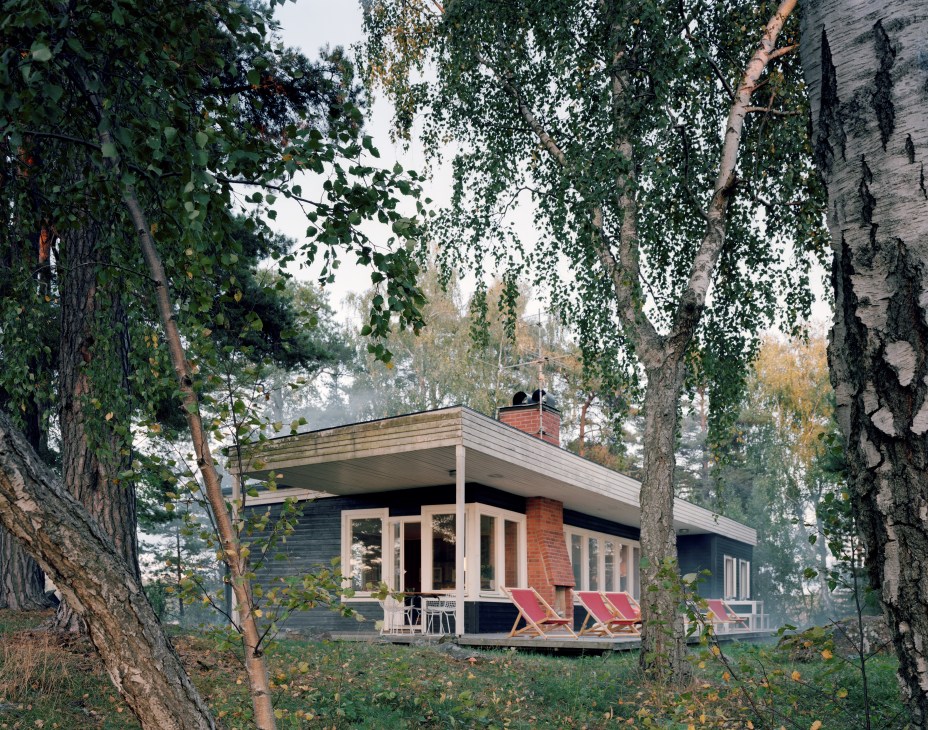 Mid-century single-storey house with brick chimney nestled among birch and pine trees in Swedish archipelago.
