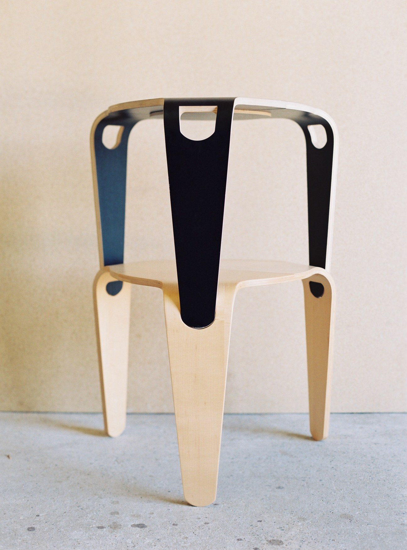 Jon Goulder's Stak stool with light wooden legs and black seat back against white wall.