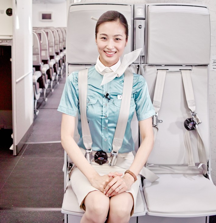 Korean Air flight attendant sitting in jumpseat wearing light blue uniform in aircraft cabin.