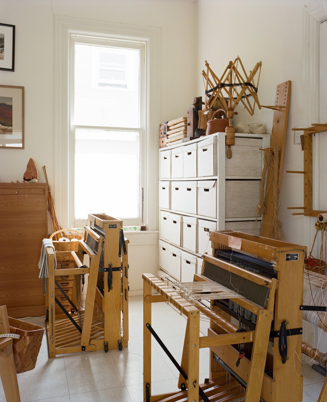Kay Sekimachi's weaving studio with wooden looms, storage shelves, and weaving materials near a bright window.
