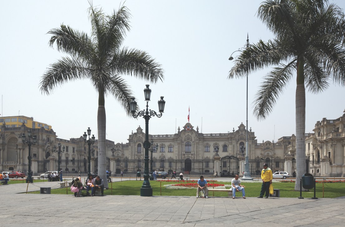 Lima's Palacio de Gobierno, Peru's presidential palace, with palm trees and people in the plaza.