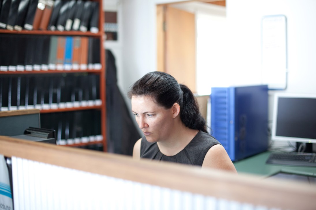 Woman working at desk in Gulf News office with shelving and computer equipment visible