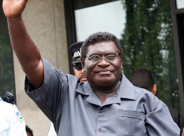Man in grey shirt waving hand outside building