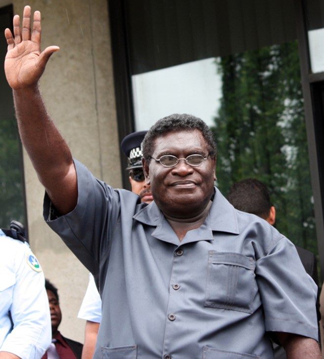 Man in grey shirt waving hand outside building