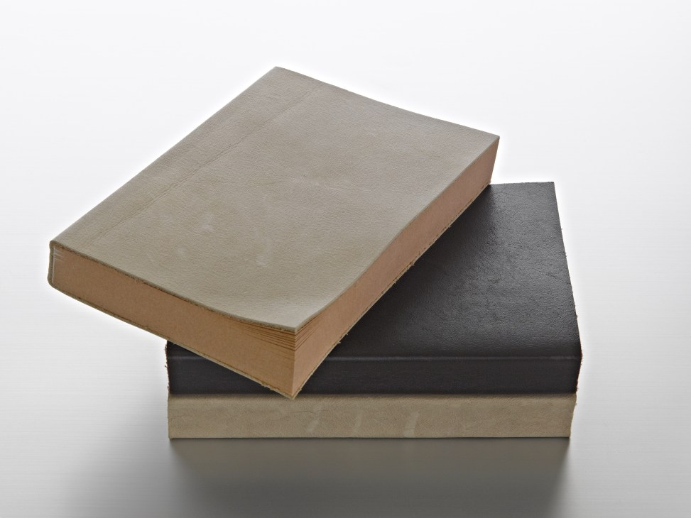 Three stacked notebooks with leather covers in cream, black, and tan colors.