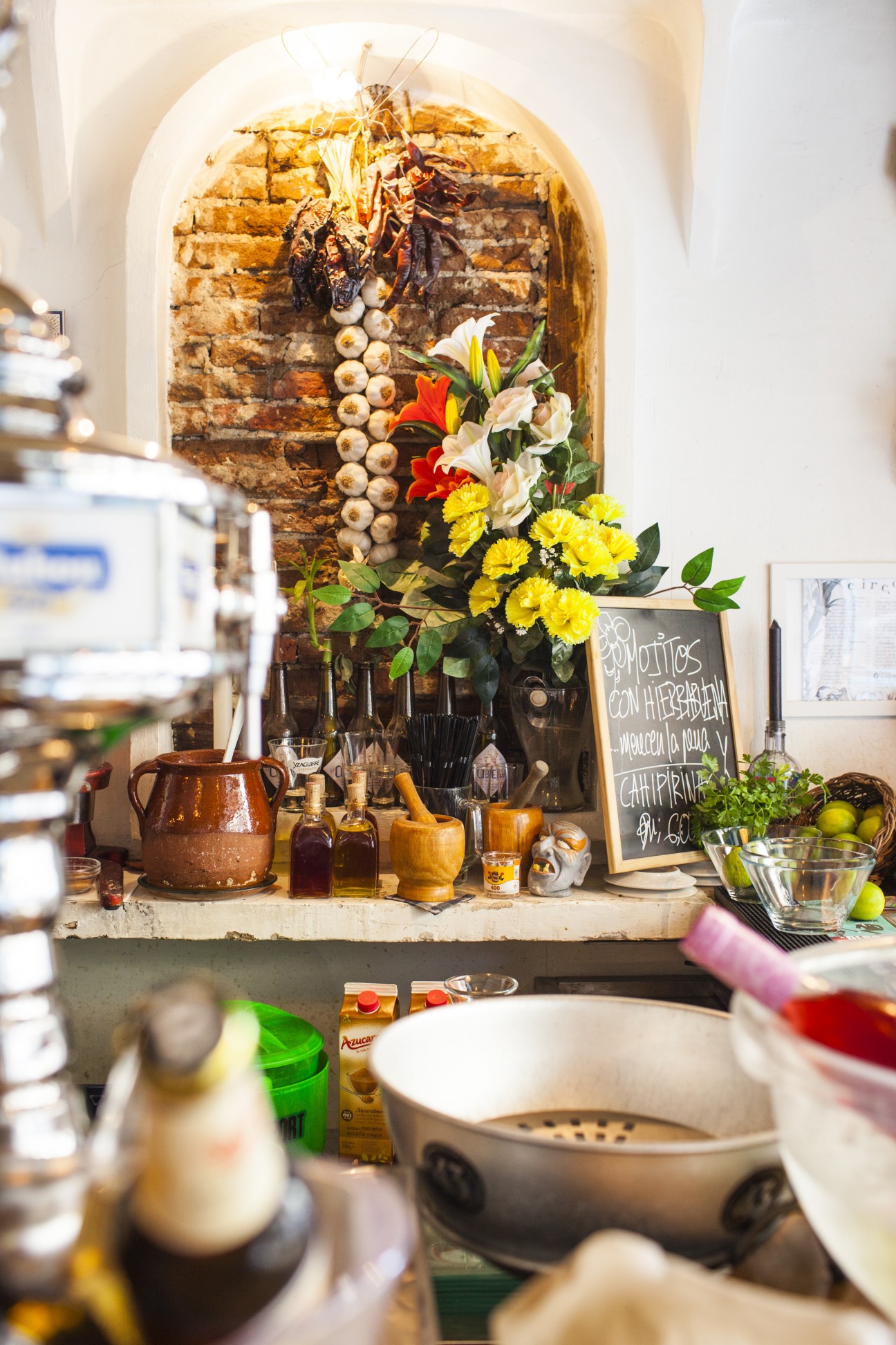 Interior of El Circo de las Tapas restaurant showing rustic brick alcove with flowers, cooking implements and bottles.