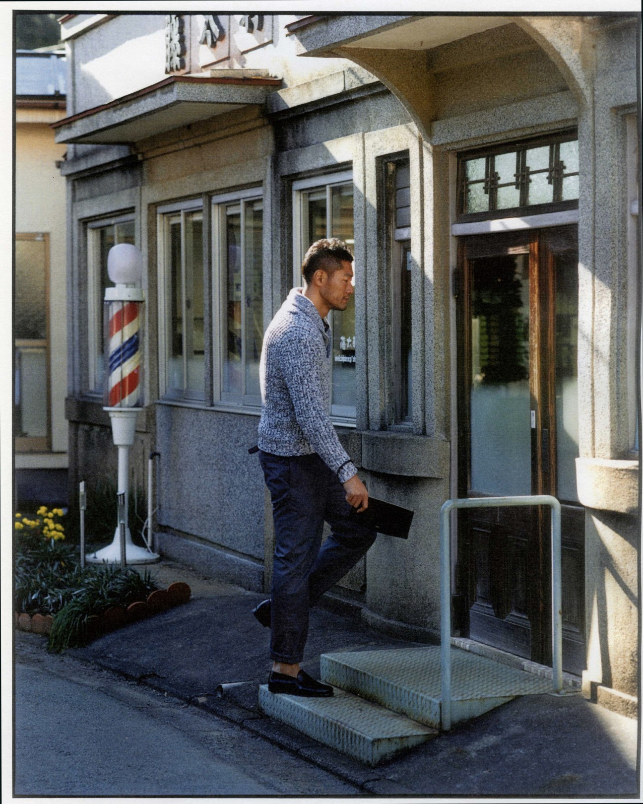 Man in blue knit jumper standing outside Totaken barber shop with traditional barber pole visible.