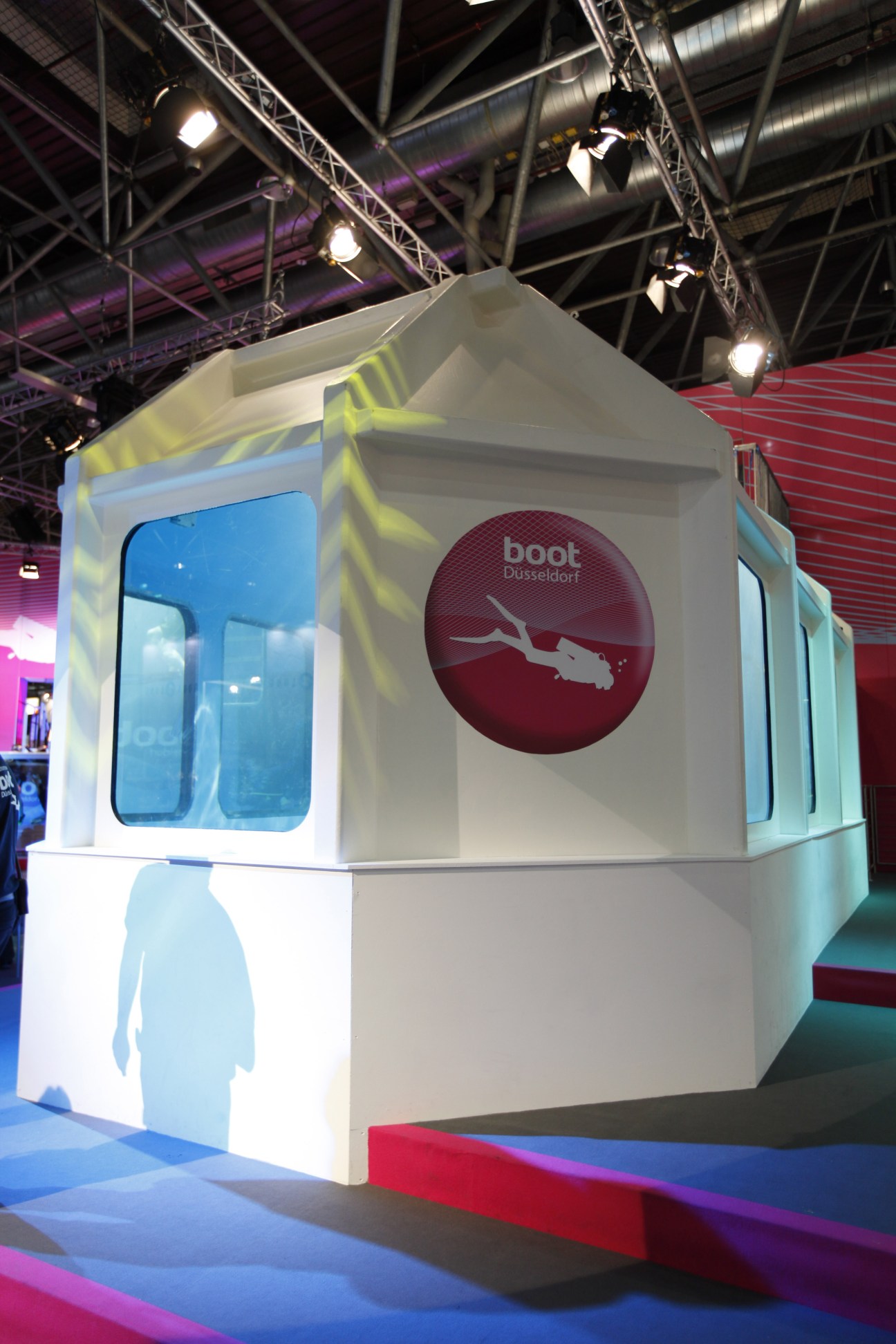 White vitrine display cube at Boot Düsseldorf with blue-tinted windows and diving silhouette logo.