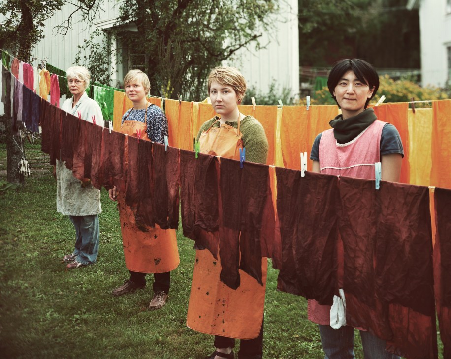 Four textile students standing behind colorful dyed fabric hanging on a clothesline to dry at Capellagården.