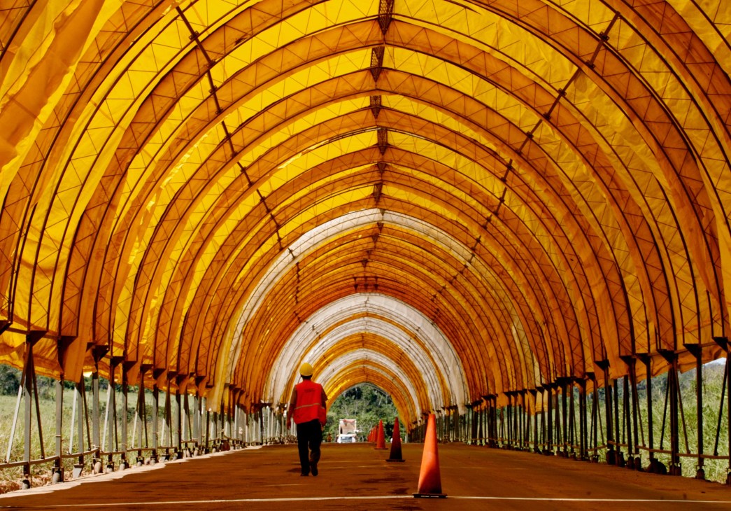 Interior of a yellow-orange greenhouse tunnel with arched ribs and black support structures stretching into the distance.