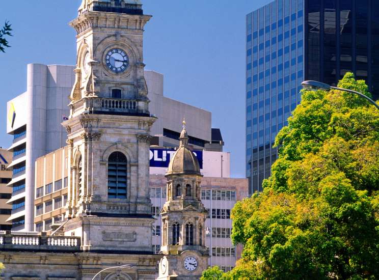 Melbourne streetscape with historic clock tower, modern buildings, and lush green trees.