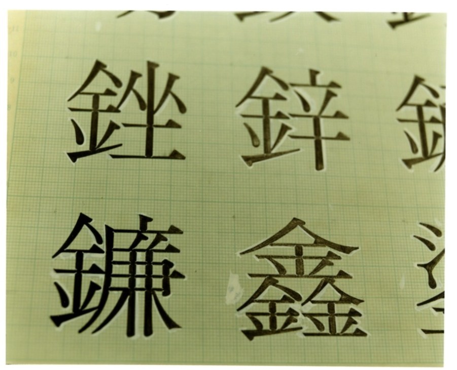 Hand-drawn Japanese kanji characters in charcoal and paint on grid paper showing font design variations.