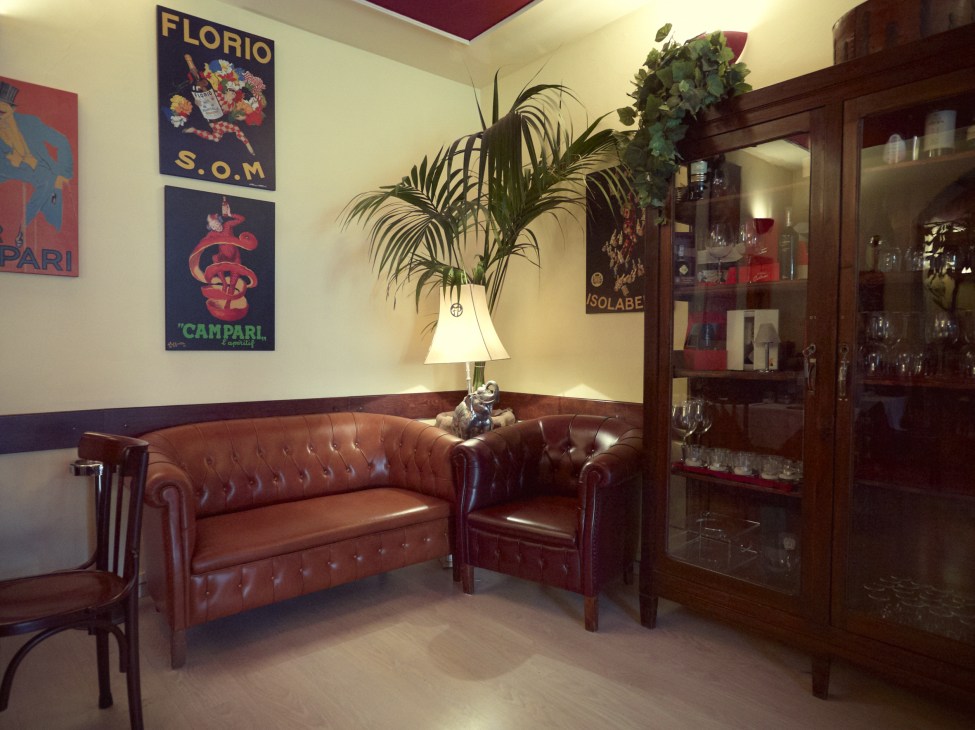 Interior of Sant'Eustorgio restaurant with burgundy leather Chesterfield sofa, vintage Italian aperitif posters, and dark wood cabinet.