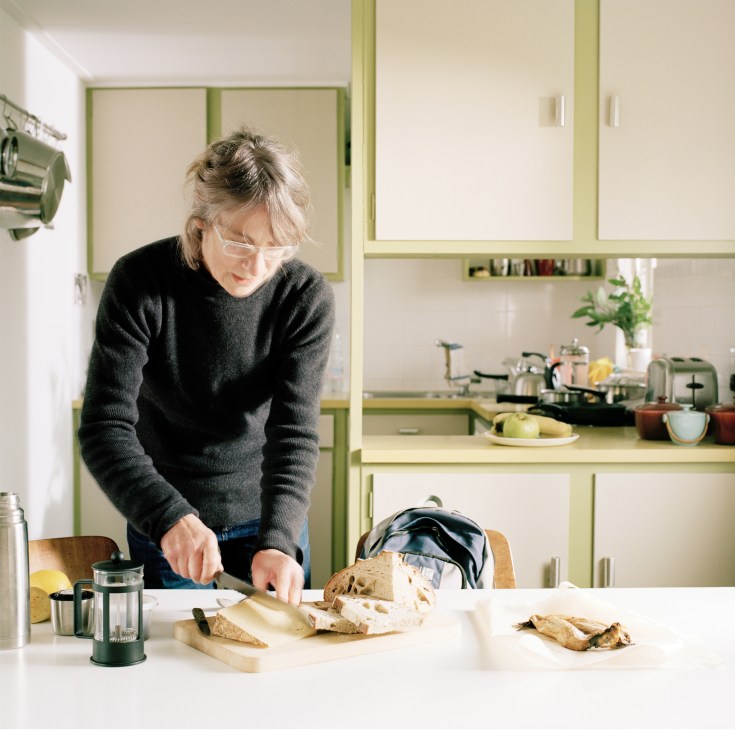Margaret Howell packs food into a black bag at her kitchen table, with bread, cheese, and other picnic items visible.