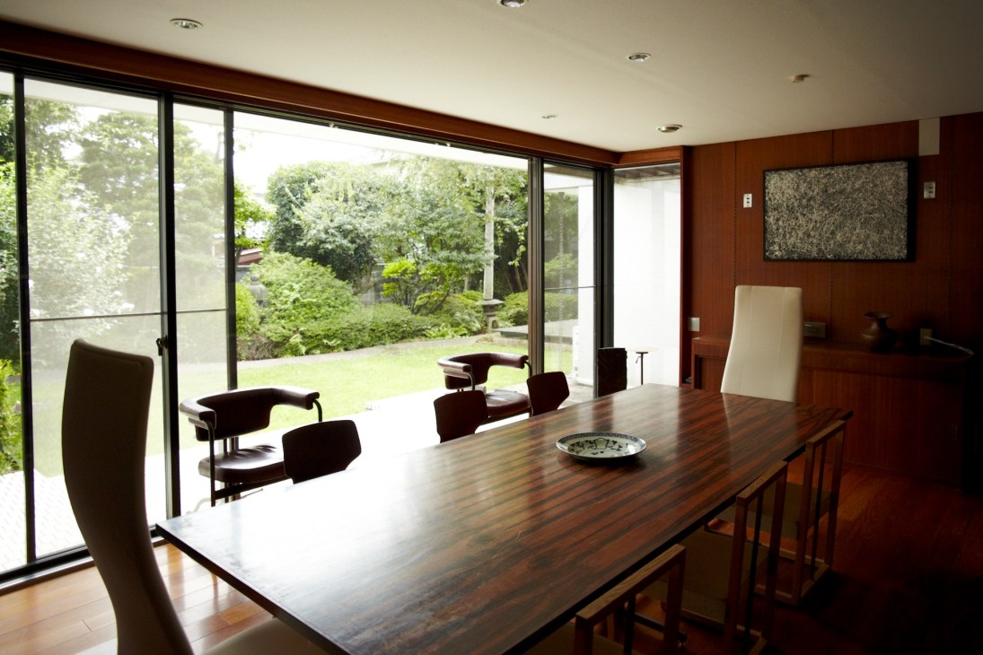 Modern boardroom with wooden table, black chairs, and floor-to-ceiling windows overlooking a garden.
