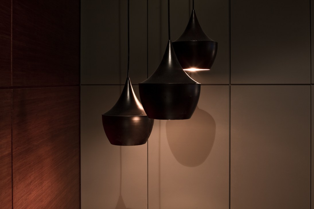 Three black pendant lights hanging against a neutral wall with wooden flooring visible.