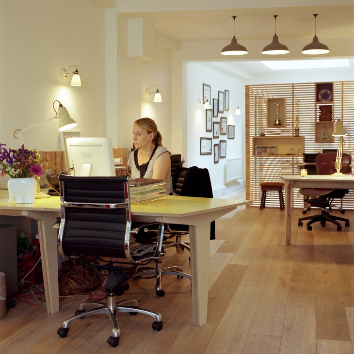 Modern office workspace with blonde wood desks, task lighting, and wooden flooring at Not To Scale animation studio in London.