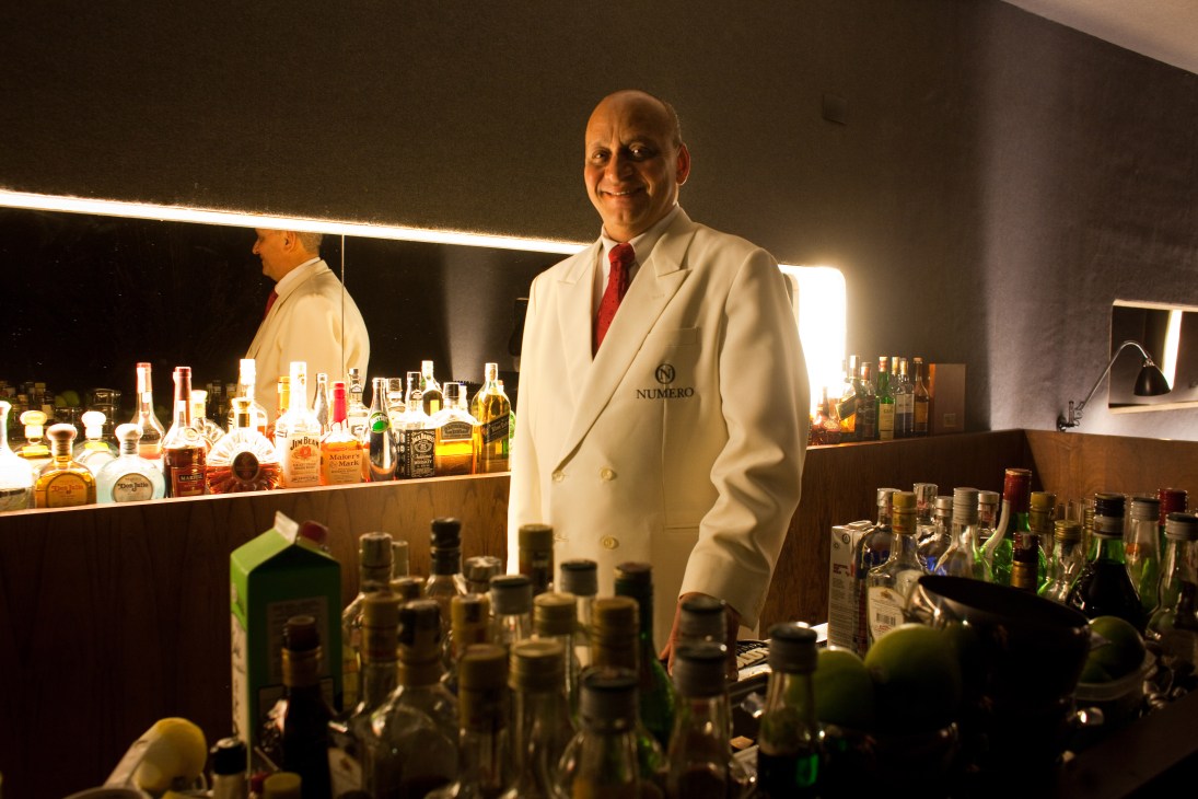 Derivan Ferreira de Souza, Numero's head barman, stands behind the bar in a white blazer with red tie.